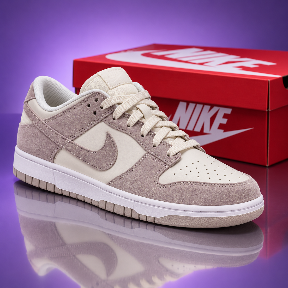 A Nike Dunk Low sneaker in beige and off-white suede and mesh, shown in front of its red Nike box on a purple reflective studio background.